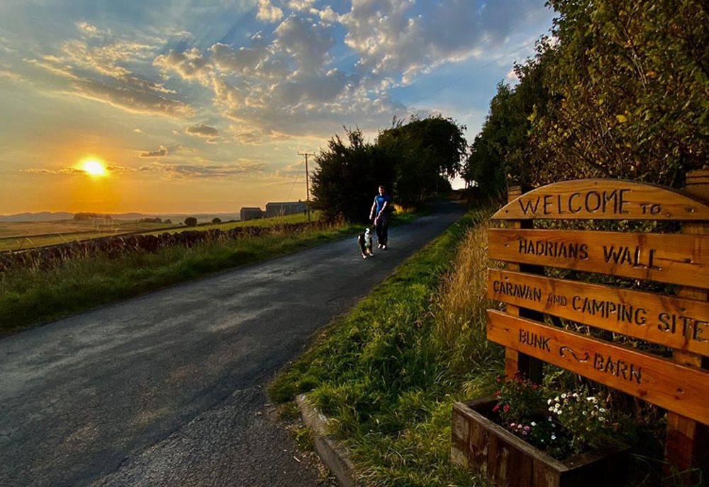 hadrians wall campsite sign with man walking dog at sunset